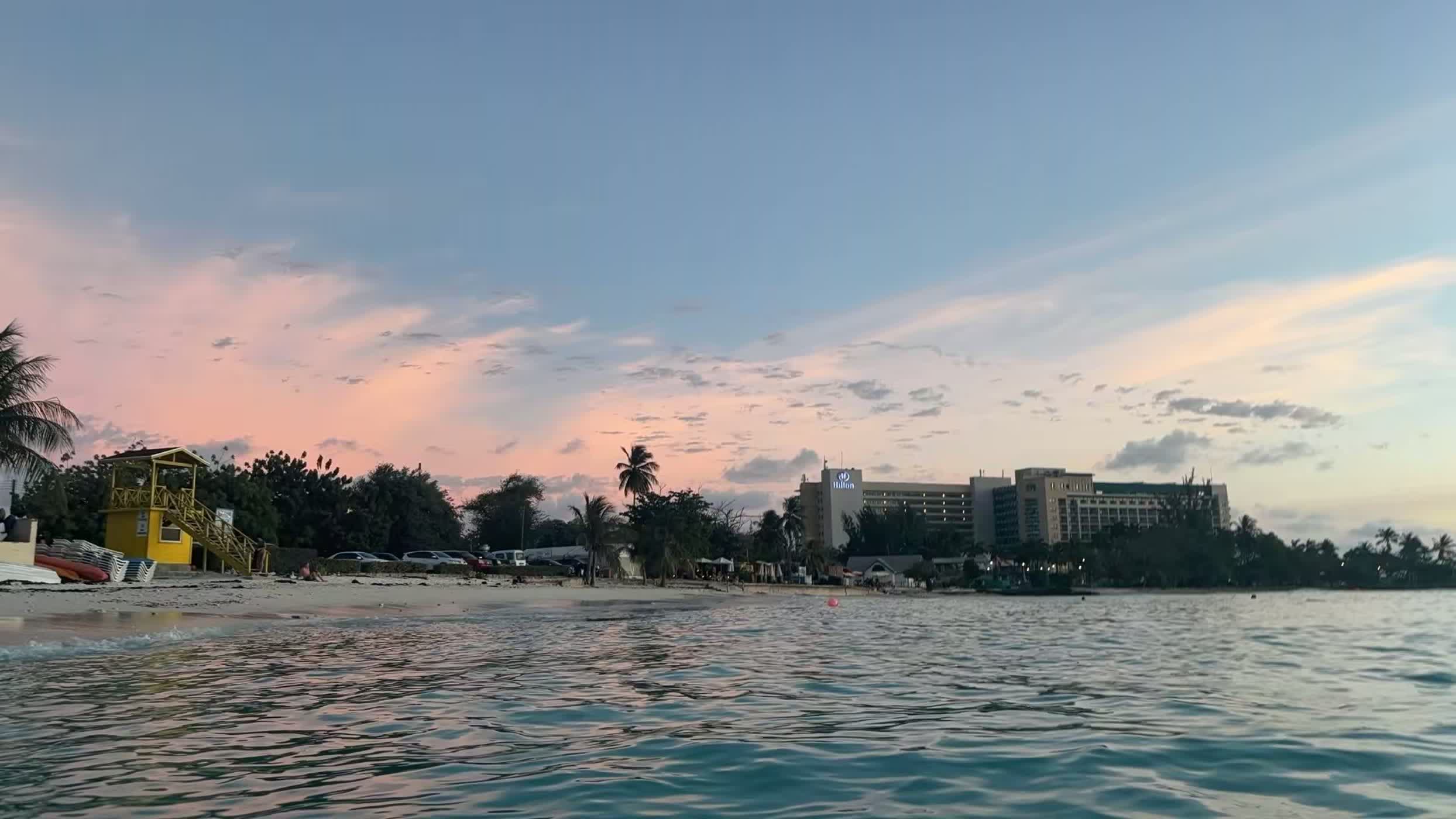 Pink dusk light over the Barbados shoreline with palms and a yellow lifeguard hut